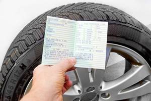 hand haelt fahrzeugschein vor winterreifen