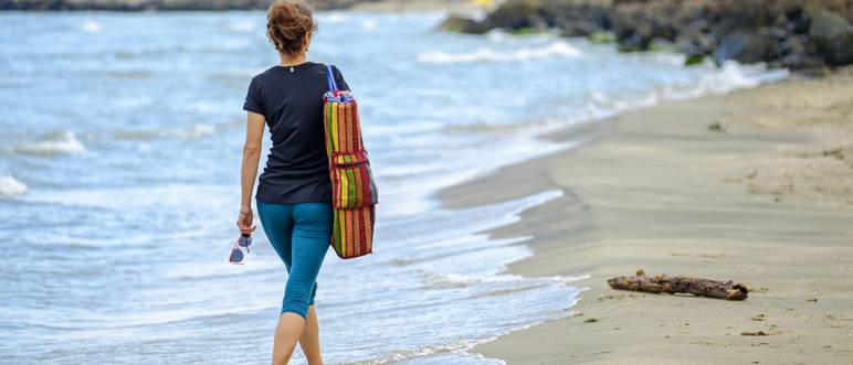 frau mit yogatasche läuft strand entlang